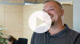 Vorschaubild des Video-Interviews mit Kevin, lachend im Büro.